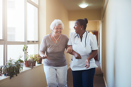 Young nursing walking down a hallway with elderly woman laughing together